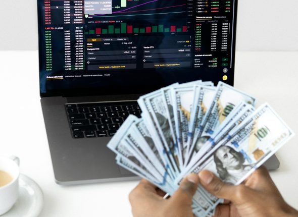 Hands holding cash in front of a laptop displaying stock market data, symbolizing financial growth and investment.